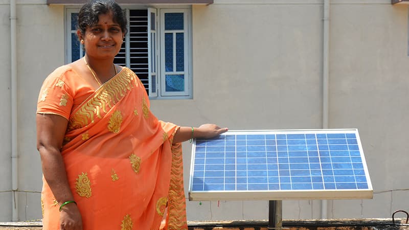 Women in bright orange dress standing next to solar panel